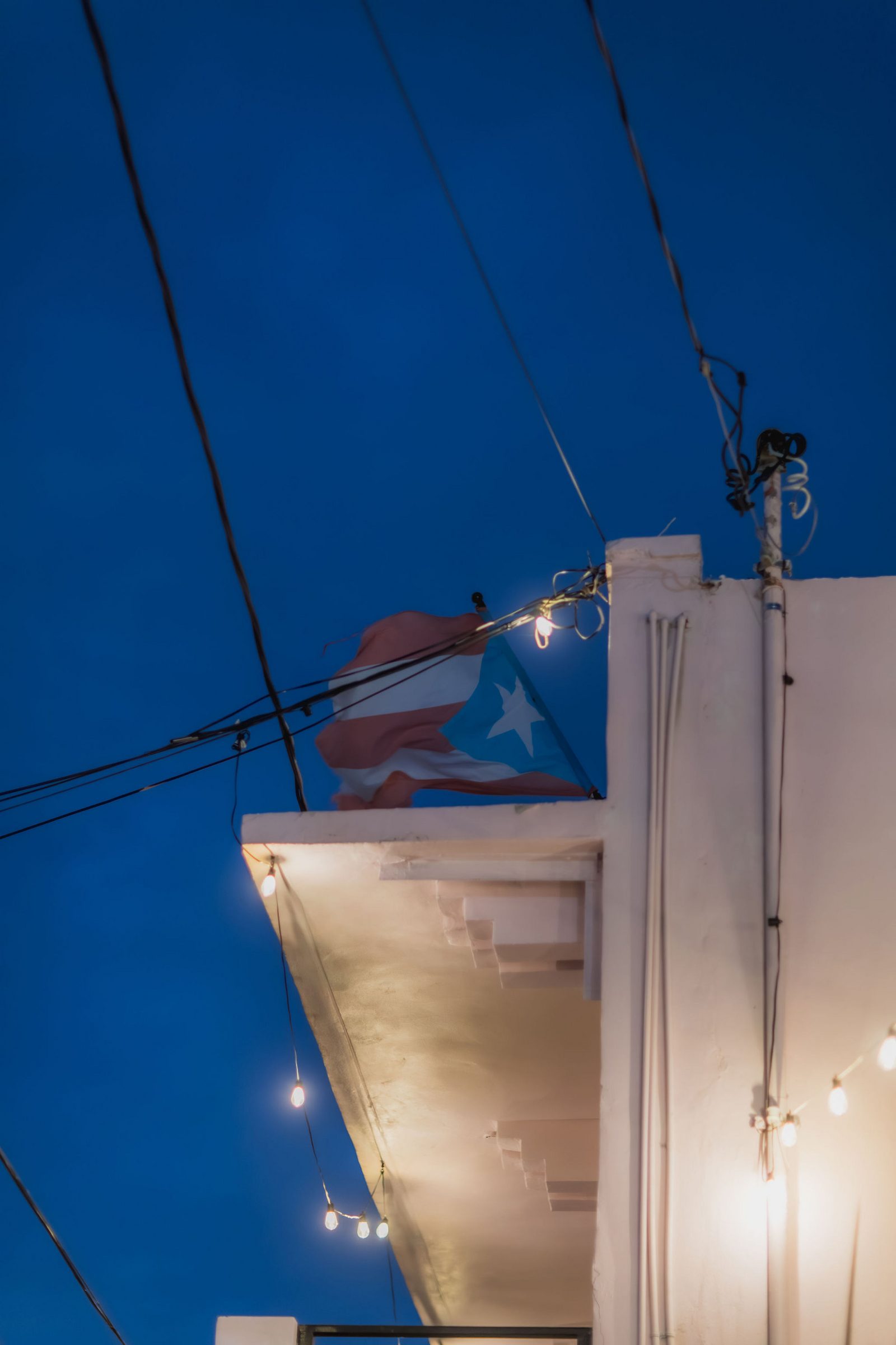 Puerto Rican flag flying over the Hotel Luz rooftop at dusk, string lights lit below
