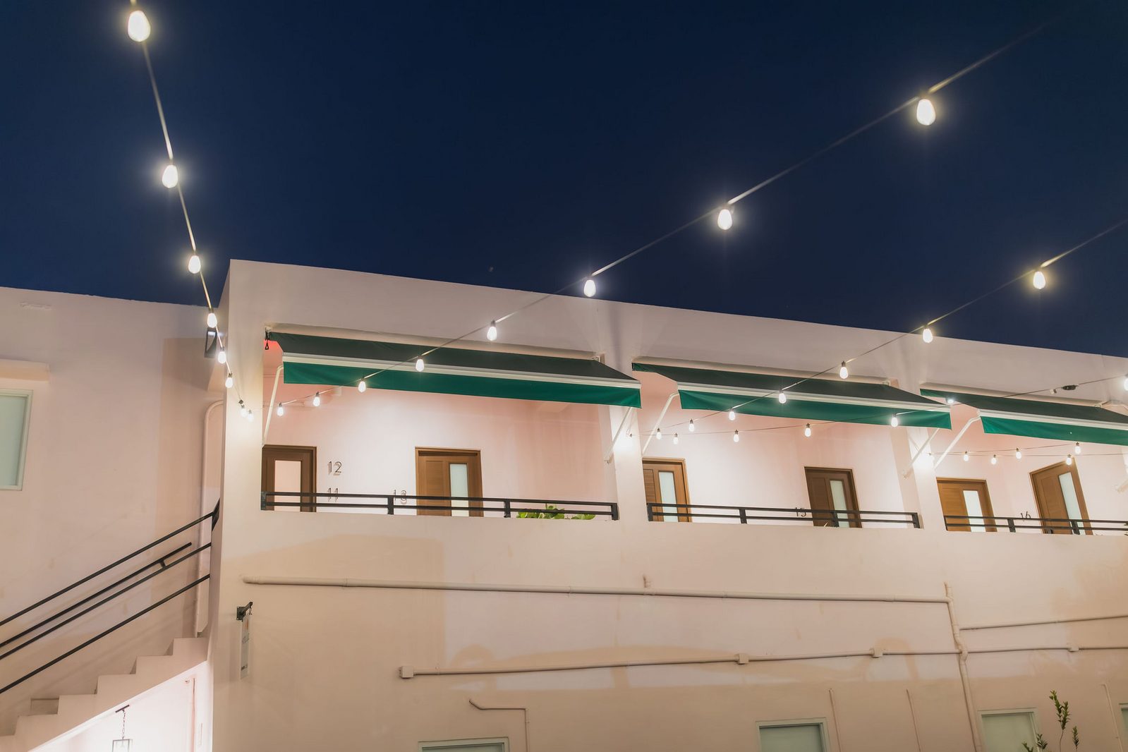 Hotel Luz balcony walkway at night with string lights and green awnings over guest room doors